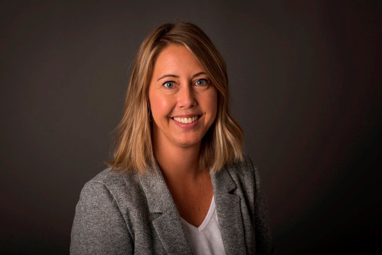 Smilende kvinne med blondt hår og grå blazer. 