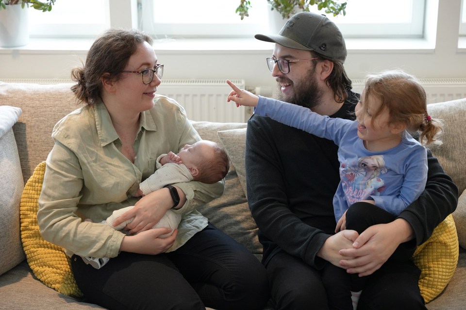 Familie på fire som sitter i en sofa, datter på fanget til far og mor holder en nyfødt baby.