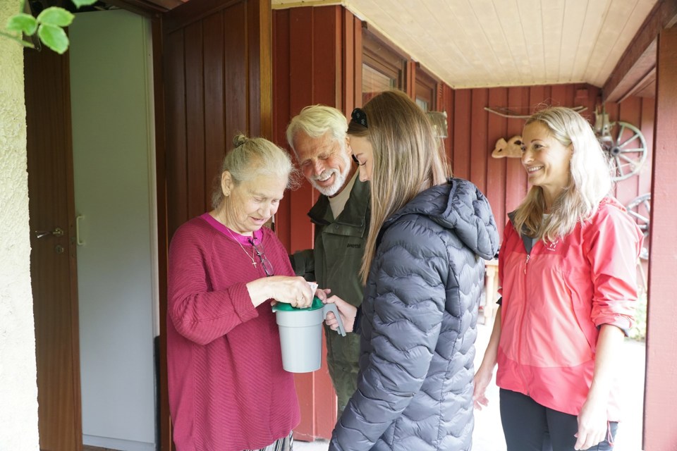 En morfar, mor og datter går med bøsse på dør. Her har en kvinne åpnet døren, og putter kontanter på bøssa.