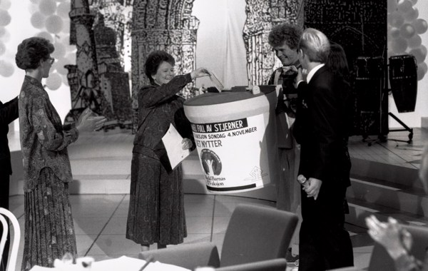 Gro Harlem Brundtland i studio i 1990, gir gave til TV-aksjonen på vegne av regjeringen. Hun putter en sjekk i en stor bøsse, og får applaus av folk rundt.